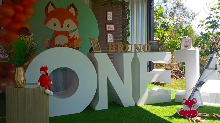 Fondo circular con zorrito del bosque en fiesta de primer año, con letras gigantes y globos naranjas