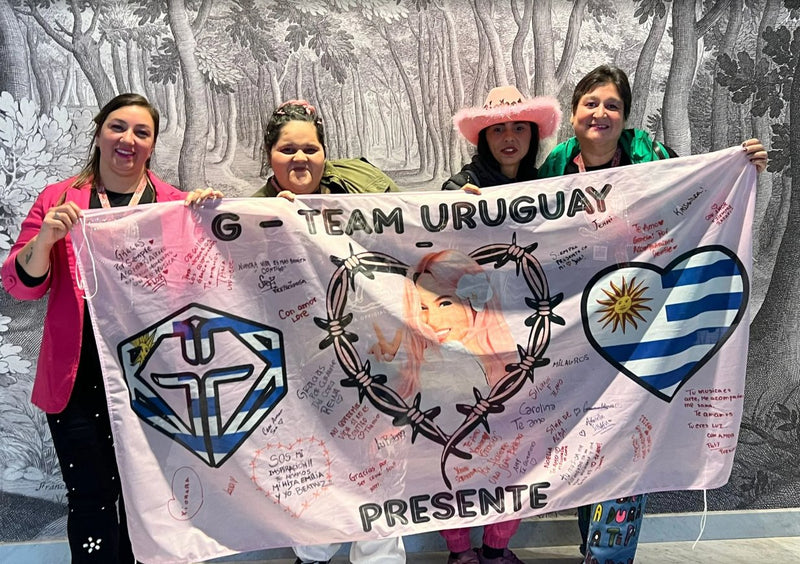 Bandera digital rosada de club de fans firmada con dedicatorias, sostenida por cuatro seguidoras