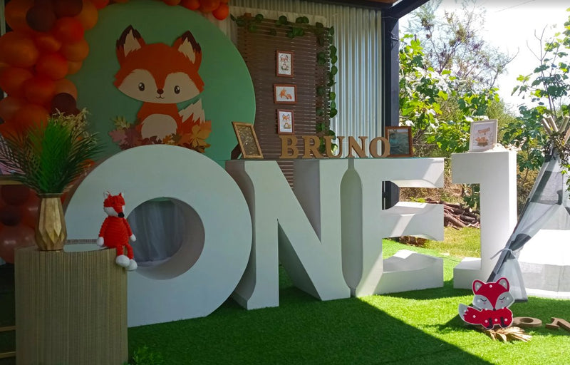 Fondo circular con zorrito del bosque en fiesta de primer año, con letras gigantes y globos naranjas