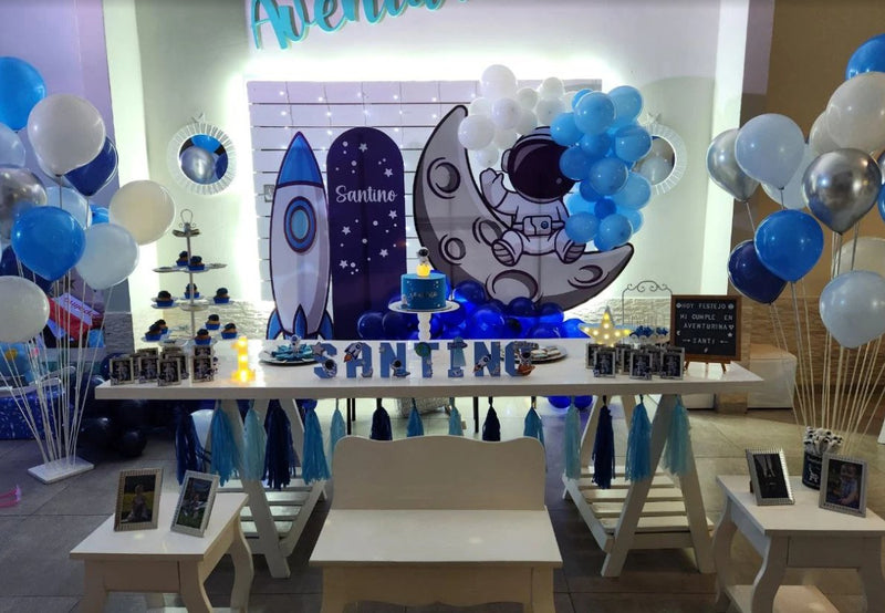 Fondo de cumpleaños temática astronauta y cohete en azul, mesa dulce con globos en salón de fiestas