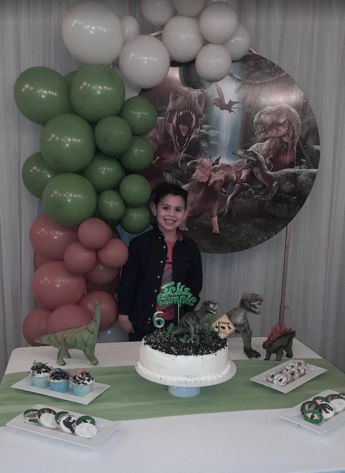 Fondo circular temática dinosaurios en cumpleaños infantil con globos verdes y rosas y mesa dulce