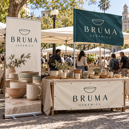 Imagen conceptual del Pack Feria BRUMA Cerámica: roll up con base de aluminio, bandera rectangular con vaina lateral en asta y lona reforzada con ojales al frente de la mesa, en una feria uruguaya.