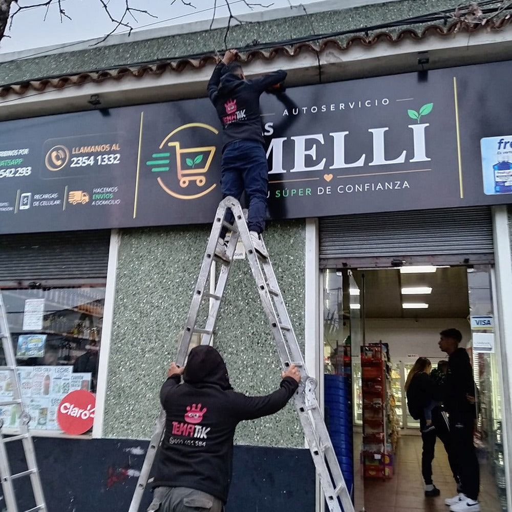 Instalación de una lona de Las Melli en una fachada, con trabajadores y escalera.