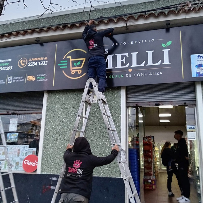 Instalación de una lona de Las Melli en una fachada, con trabajadores y escalera.