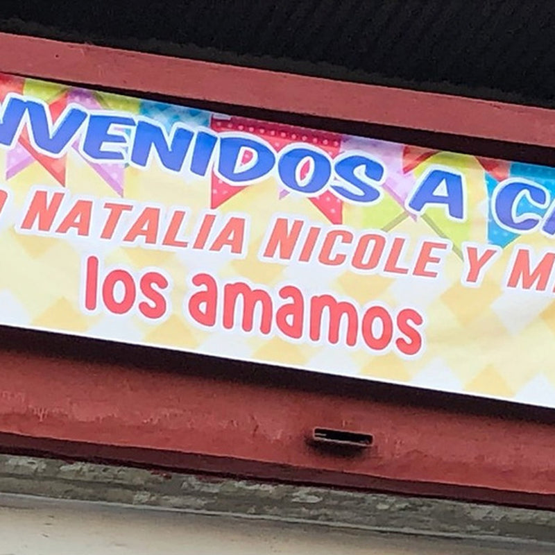 Pasacalle Bienvenidos a casa para Pablo, Natalia, Nicole y Melany, instalado sobre una fachada.