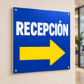 Imagen conceptual de un cartel de señalética en Sintra azul con la palabra «RECEPCIÓN» y una flecha amarilla impresas, montado en pared con canto blanco visible.